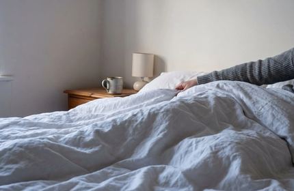 Lenzuola di lino sgualcite nella luce del mattino, con una persona ancora a letto sotto le coperte.