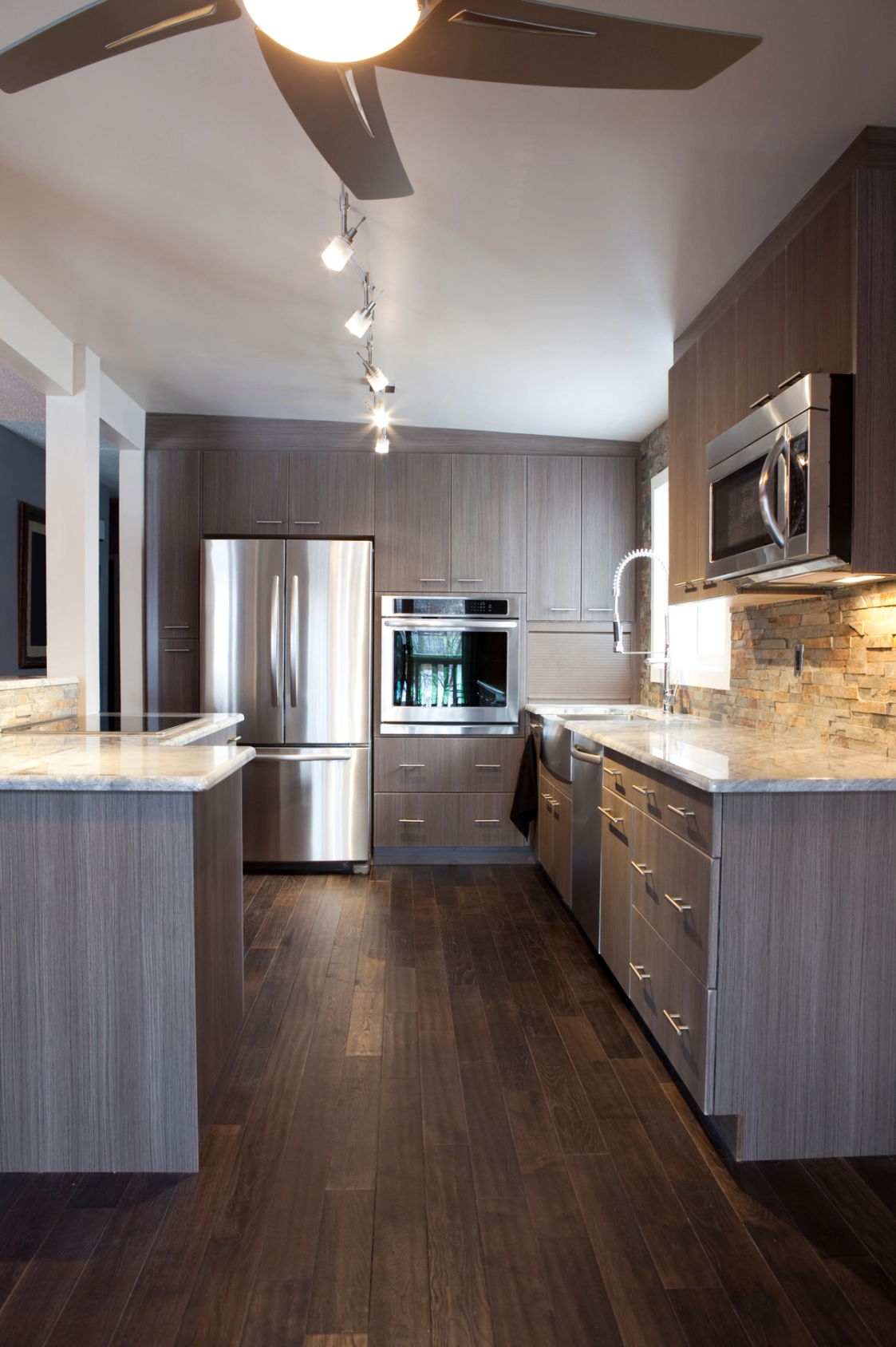 A modern kitchen with dark wood cabinets, stainless steel appliances, and a stone backsplash.