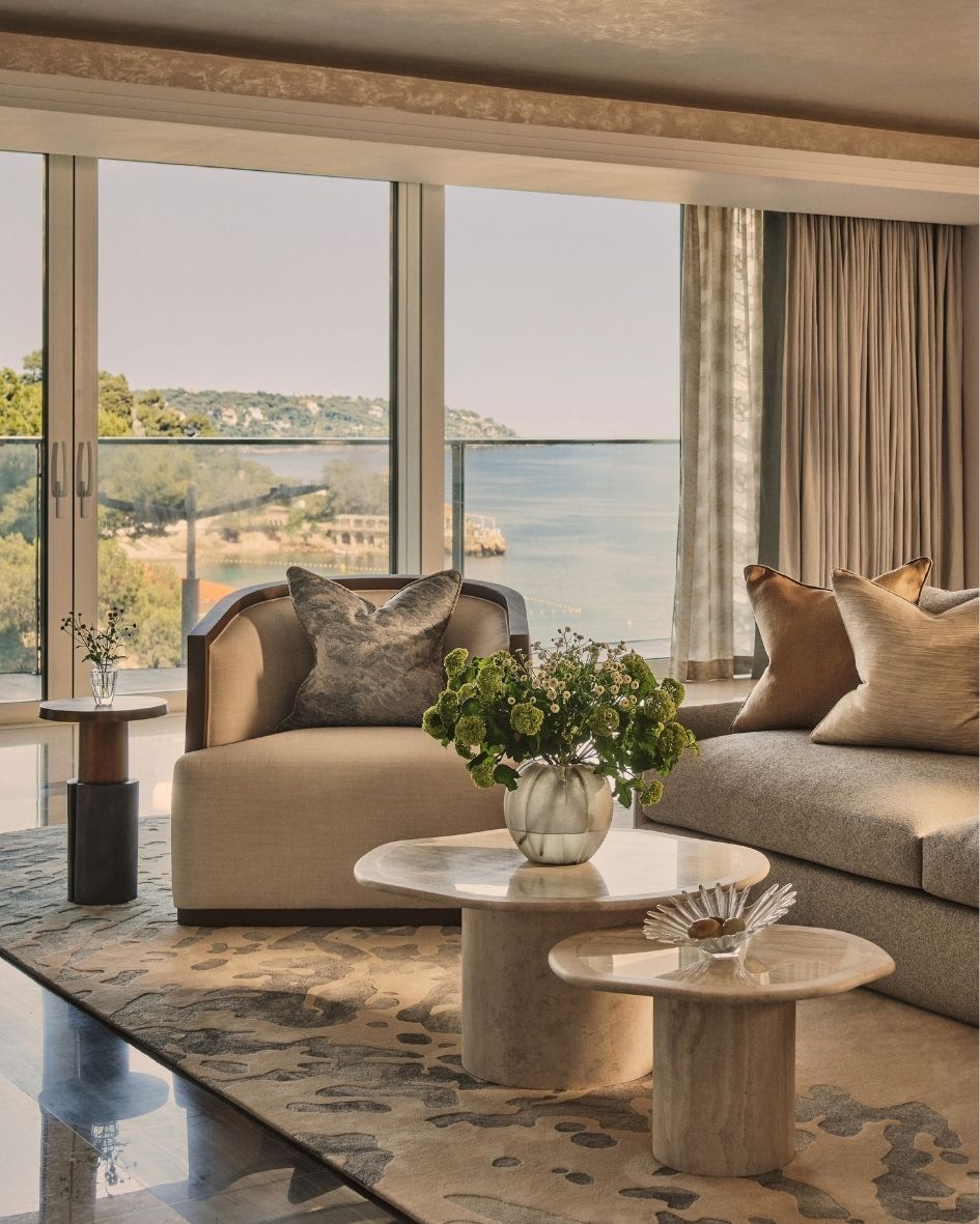 Luxury coastal living room with neutral upholstered seating, sculptural marble coffee tables and panoramic sea views.