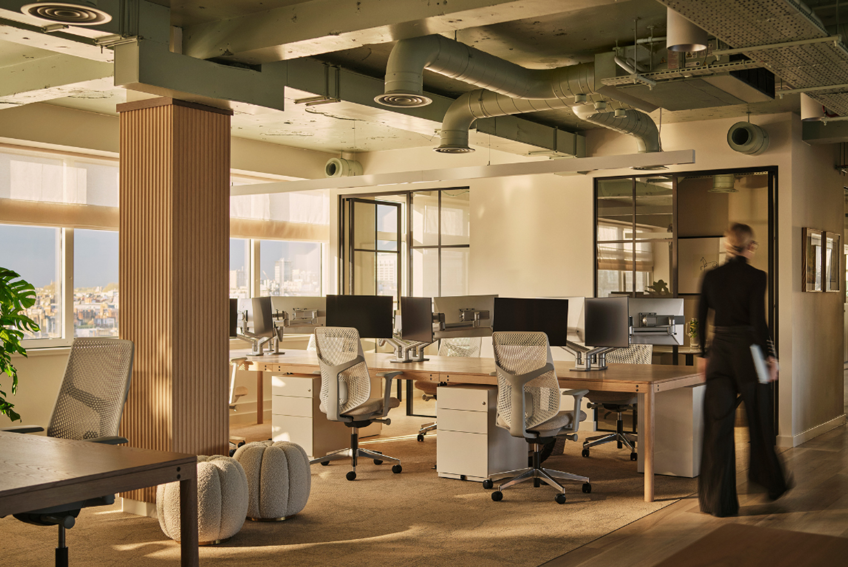 Contemporary open-plan office interior with natural wood desks, ergonomic task chairs and large windows, designed as a warm, considered workspace within a modern interior design studio.
