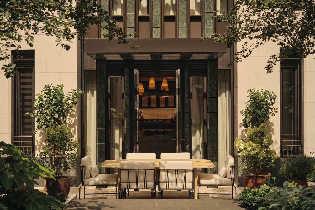 Elegant outdoor dining terrace with a wooden table, upholstered chairs and lush greenery framed by a contemporary stone façade.