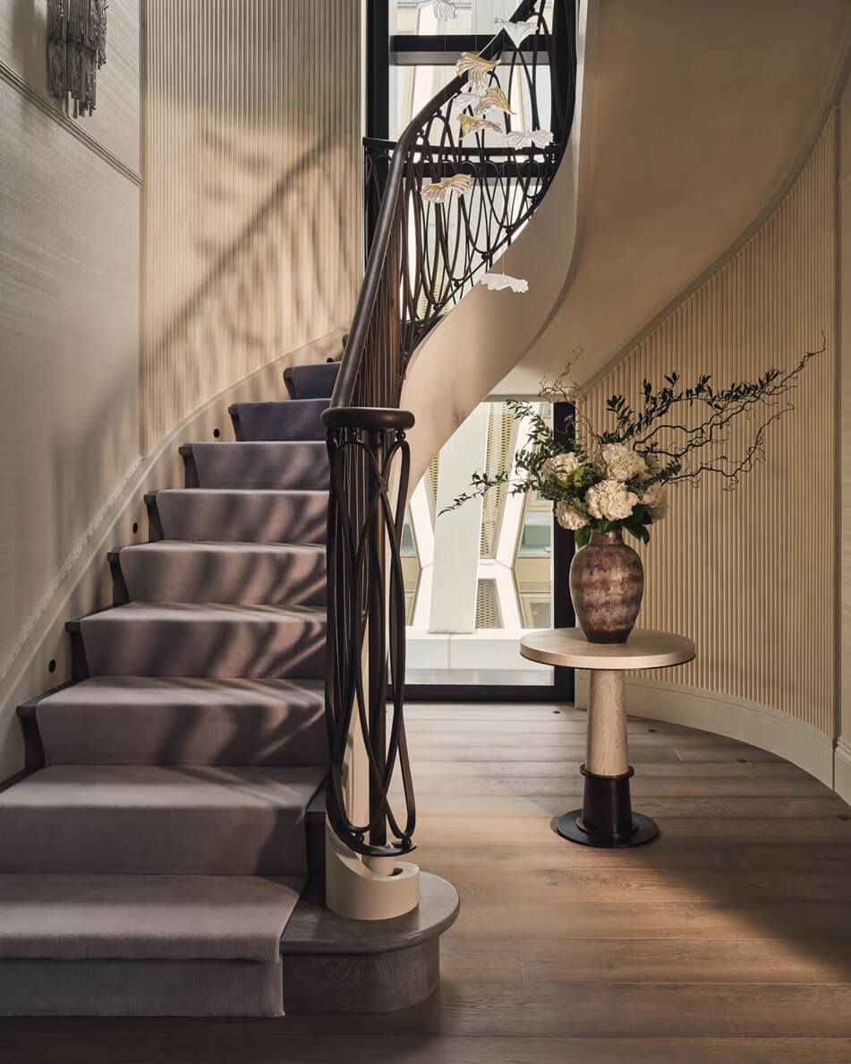 A staircase with an ombre runner, and a large vase sitting on a side table.