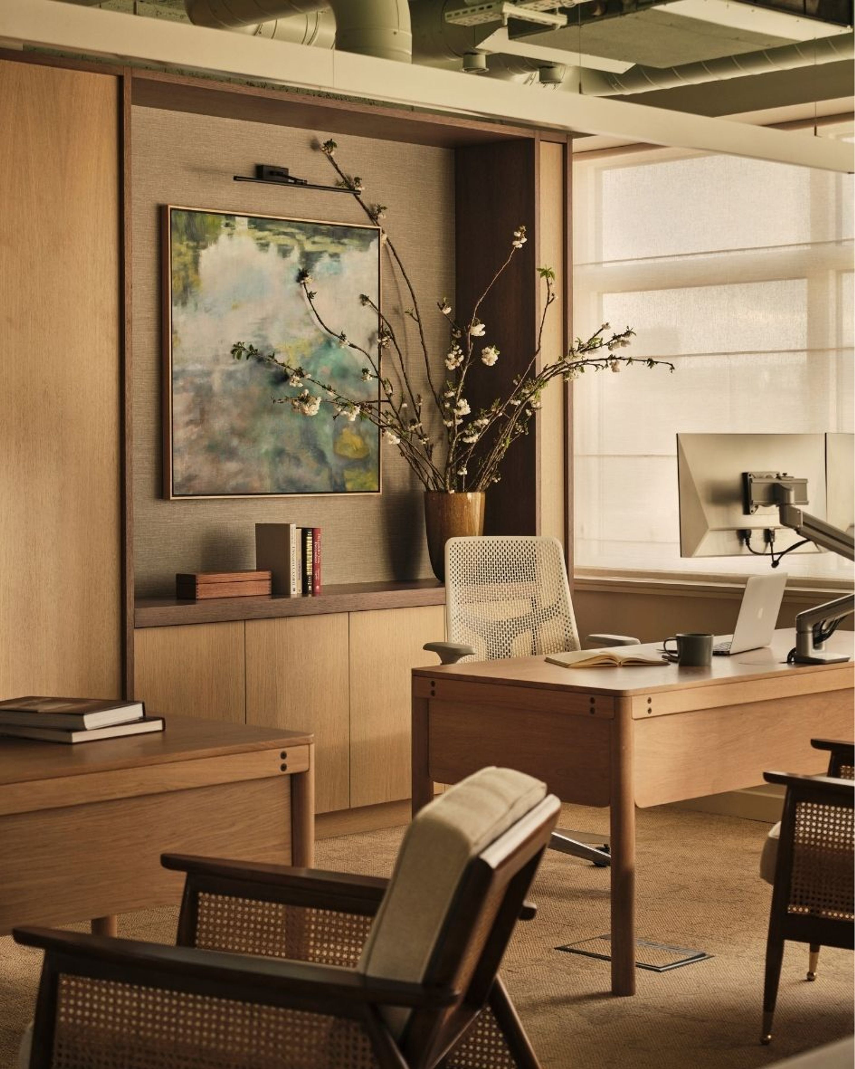 Contemporary home office featuring bespoke oak cabinetry, framed artwork, a timber desk and woven chairs in warm neutral tones.