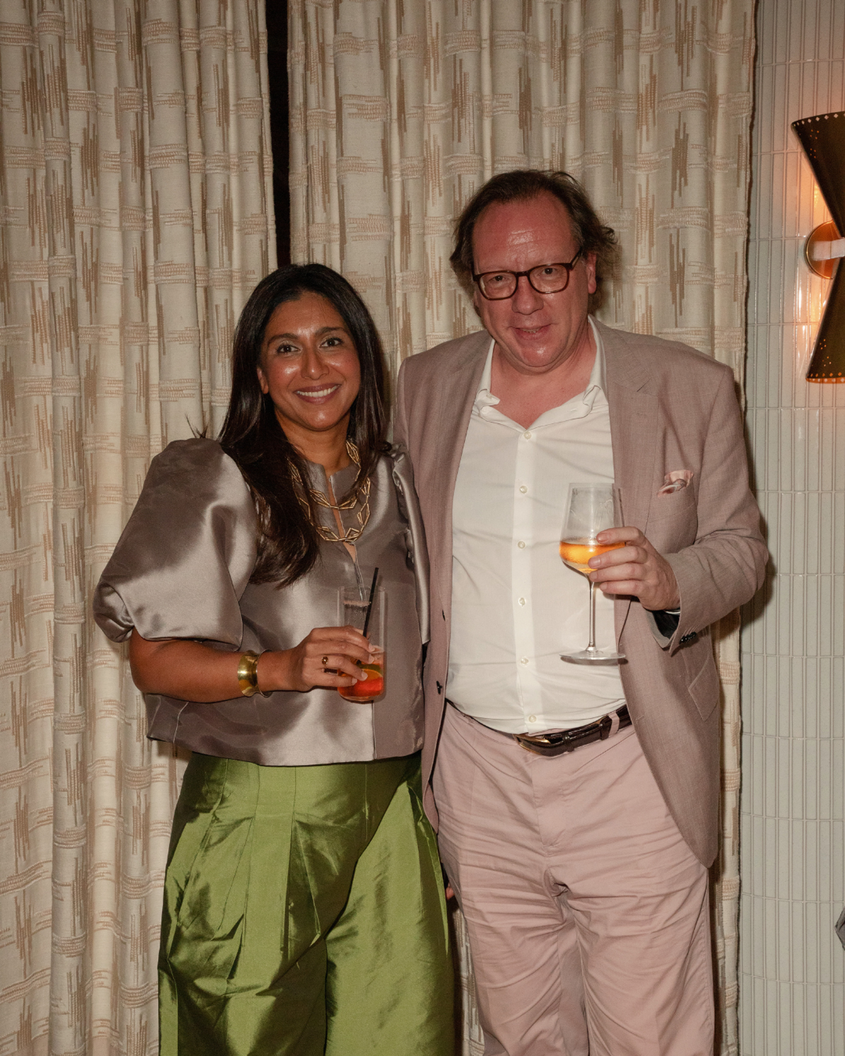 Elicyon Founder and Director Charu Gandhi with a guest at a London interior design studio event, set against patterned curtains.