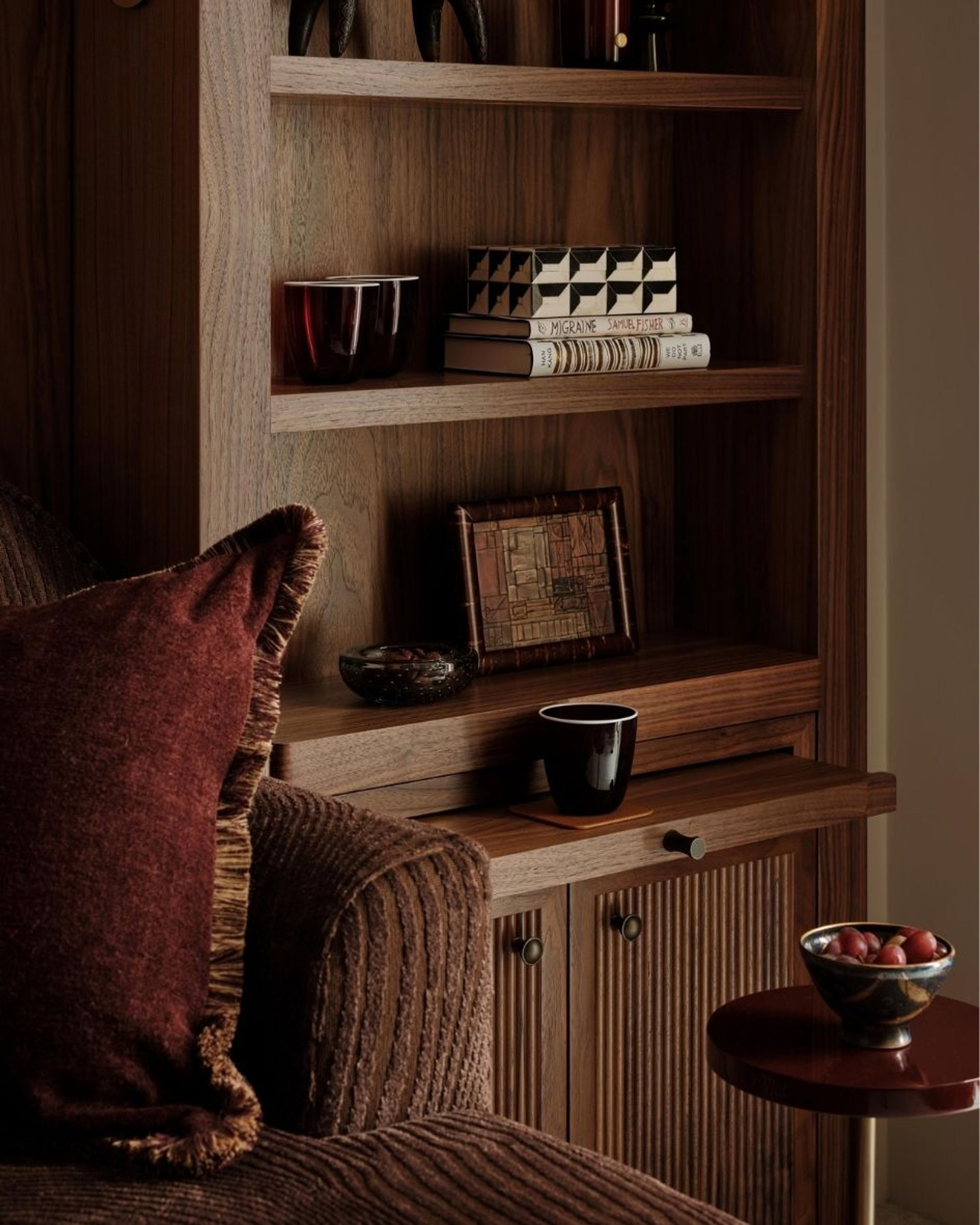 Close-up of bespoke timber shelving styled with decorative objects, books and rich burgundy textiles in a luxury residential interior.