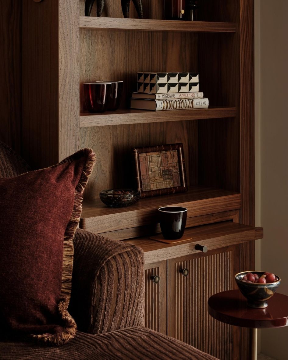 Close-up of bespoke timber shelving styled with decorative objects, books and rich burgundy textiles in a luxury residential interior.