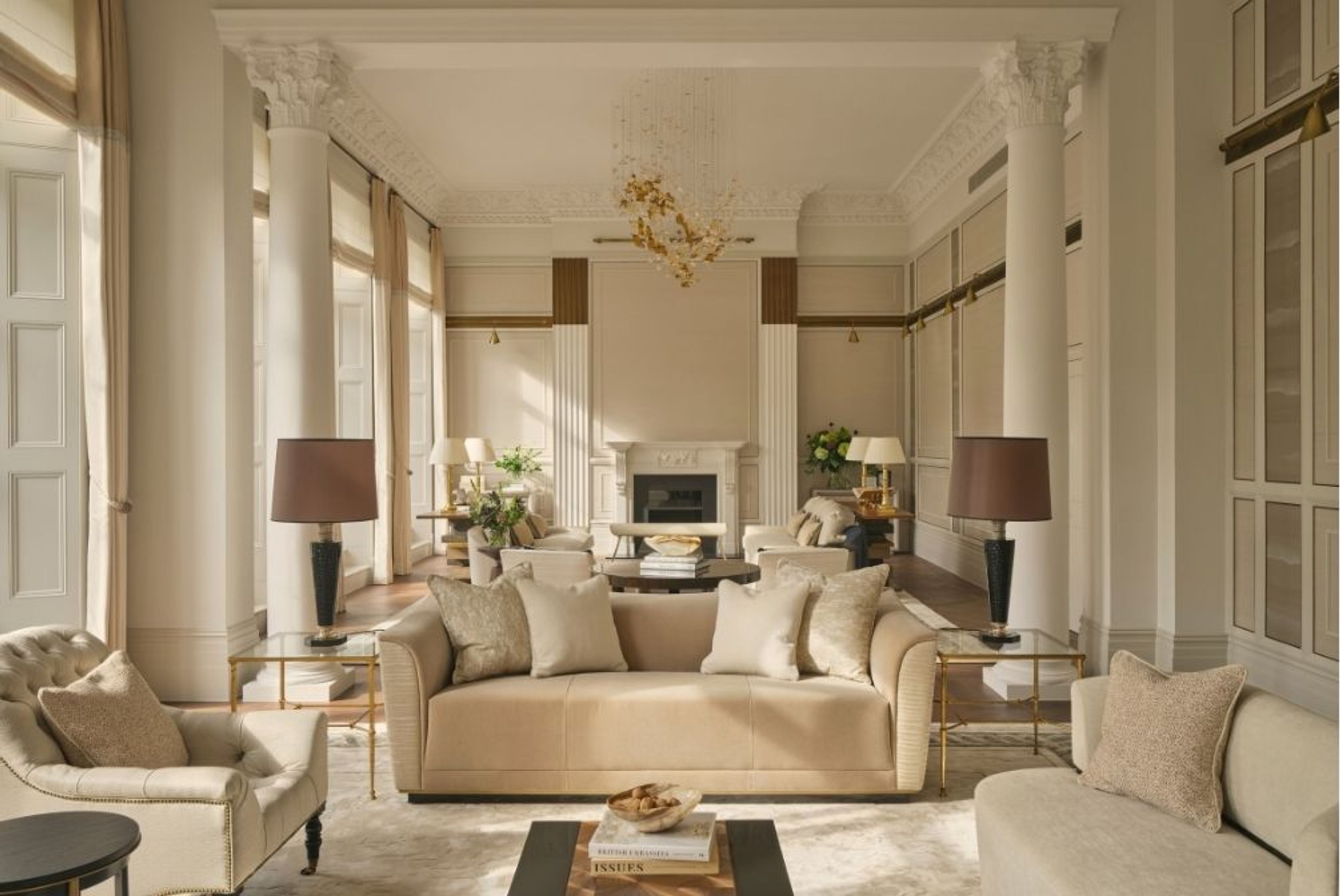 Elegant reception room featuring classical columns, decorative cornicing, neutral upholstered seating and a statement chandelier.