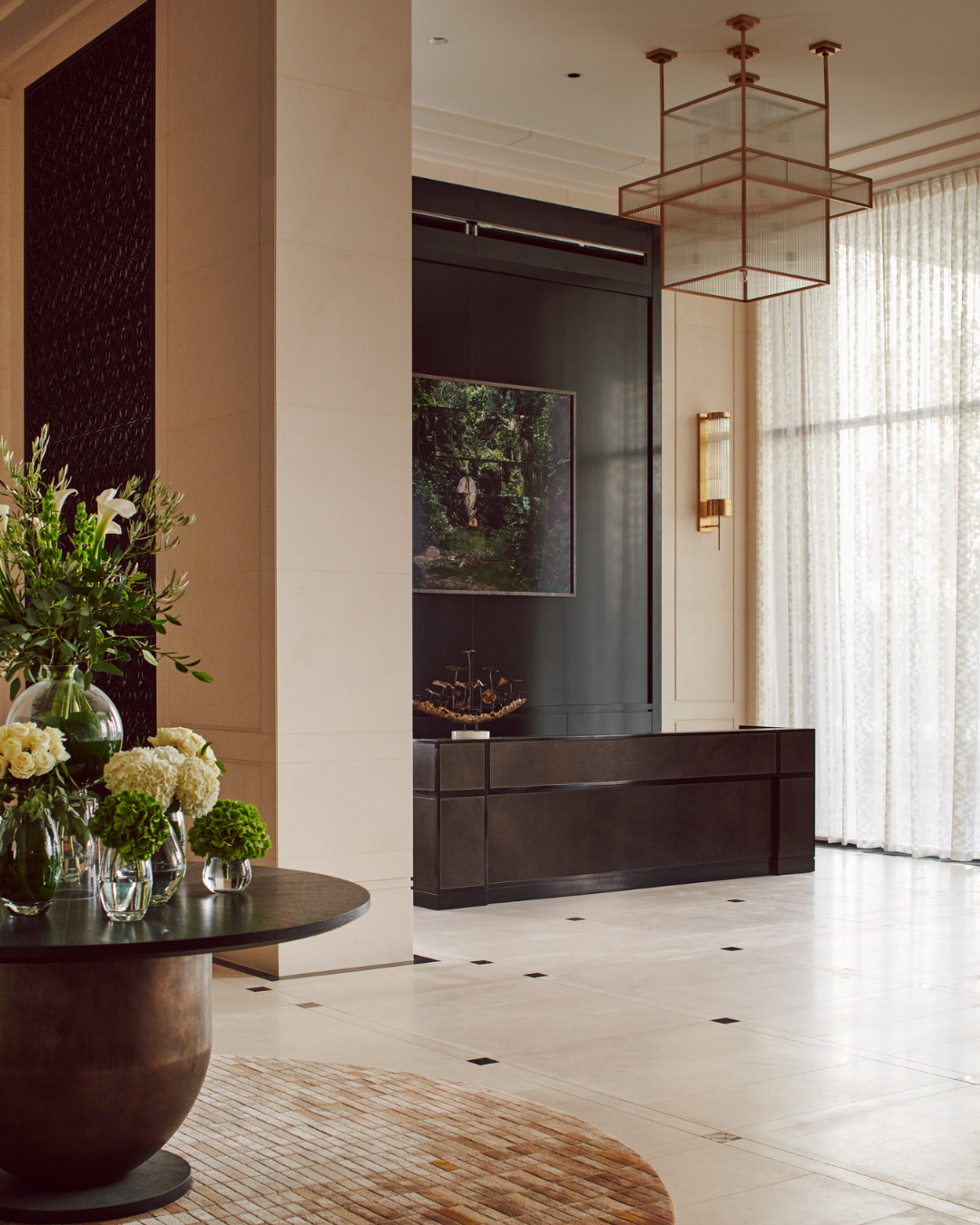 Modern interior design entrance hall with sculptural pendant lighting, limestone flooring and dark wood cabinetry, styled with floral arrangements and sheer curtains in a refined London interior design scheme.
