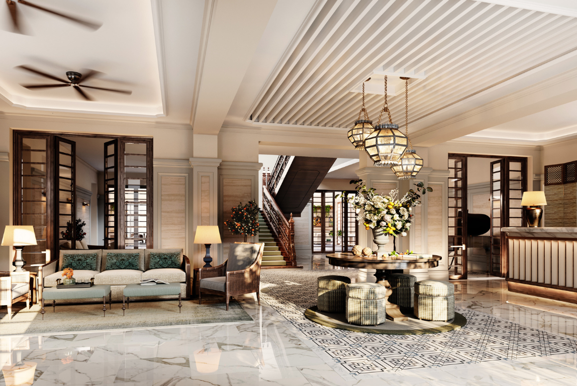 A light-filled reception space with polished marble flooring, layered seating and a central round table beneath lantern-style pendants, anchored by a sweeping staircase beyond.