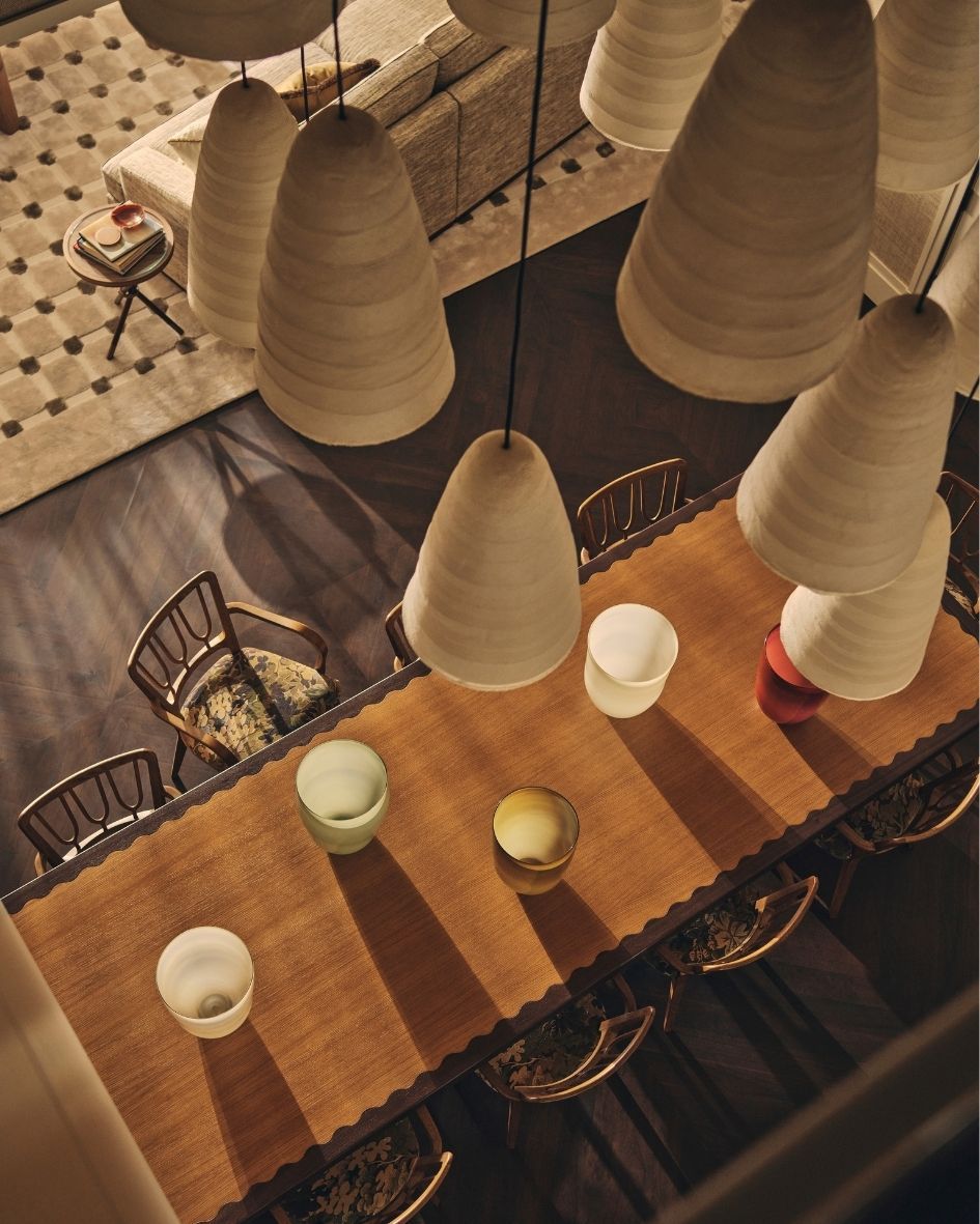 Overhead view of a contemporary dining room with a sculptural wooden table, patterned chairs and oversized pendant lighting.
