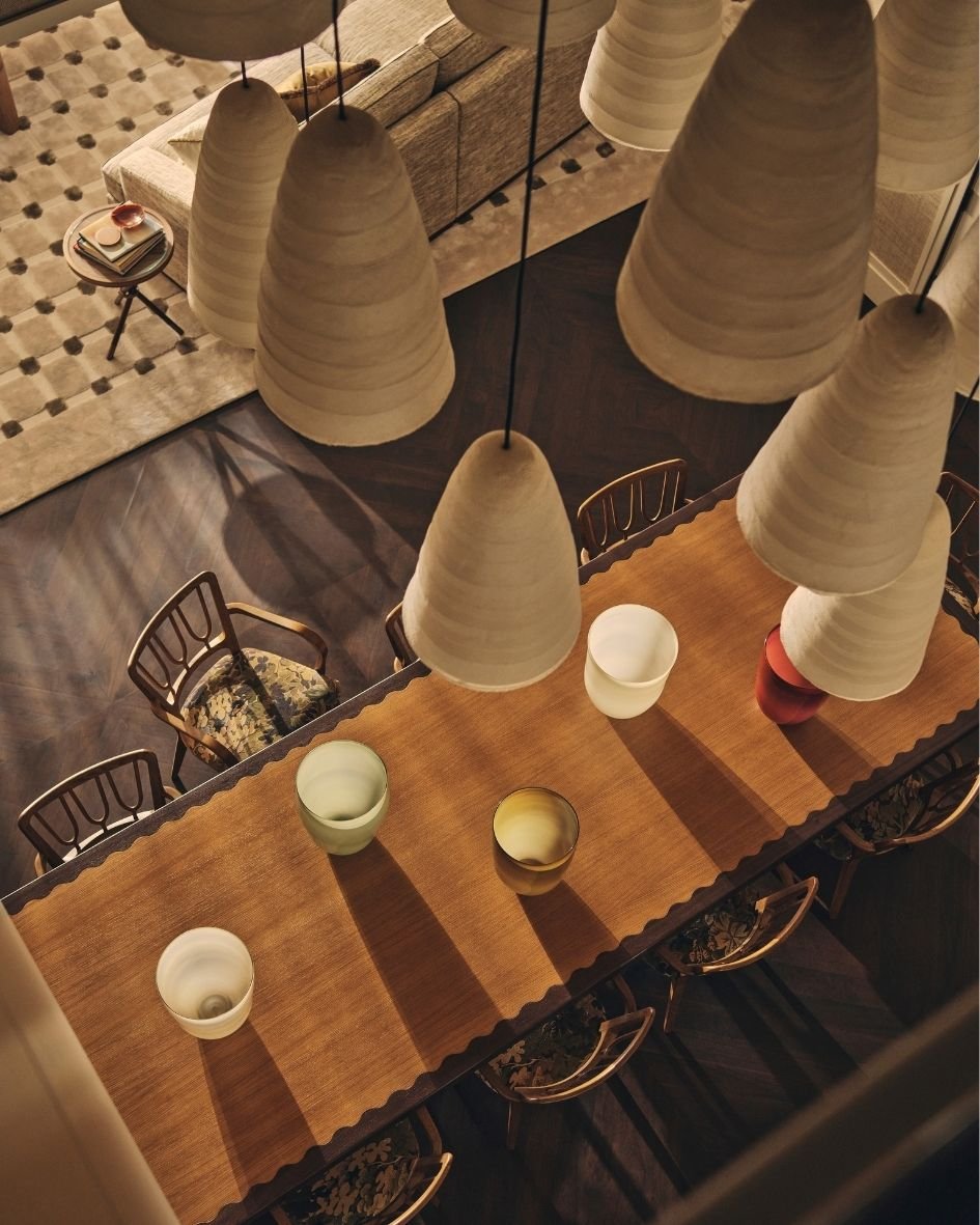 Overhead view of a contemporary dining room with a sculptural wooden table, patterned chairs and oversized pendant lighting.