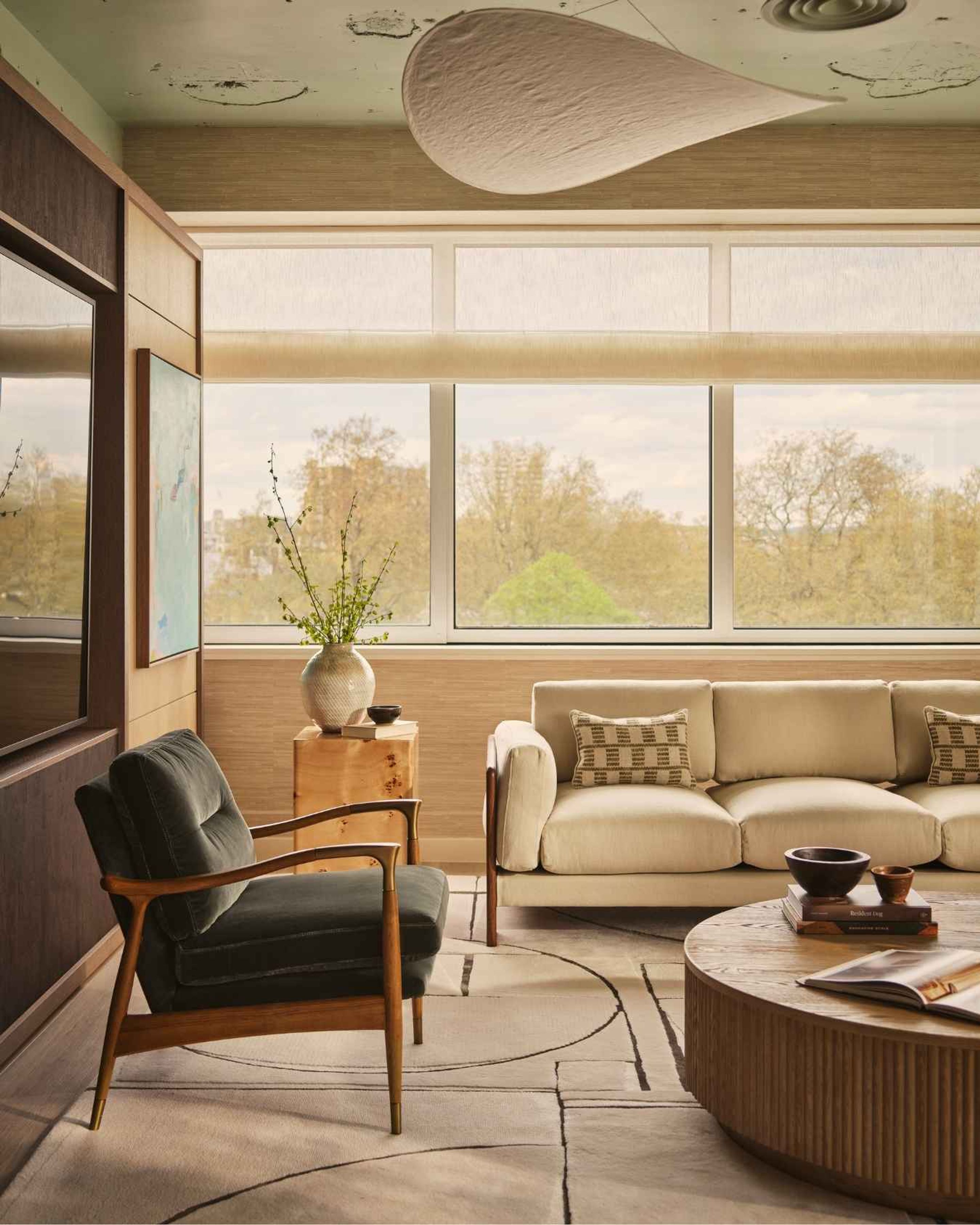 Elegant contemporary lounge with cream sofa, timber detailing, sculptural lighting and large windows overlooking greenery.