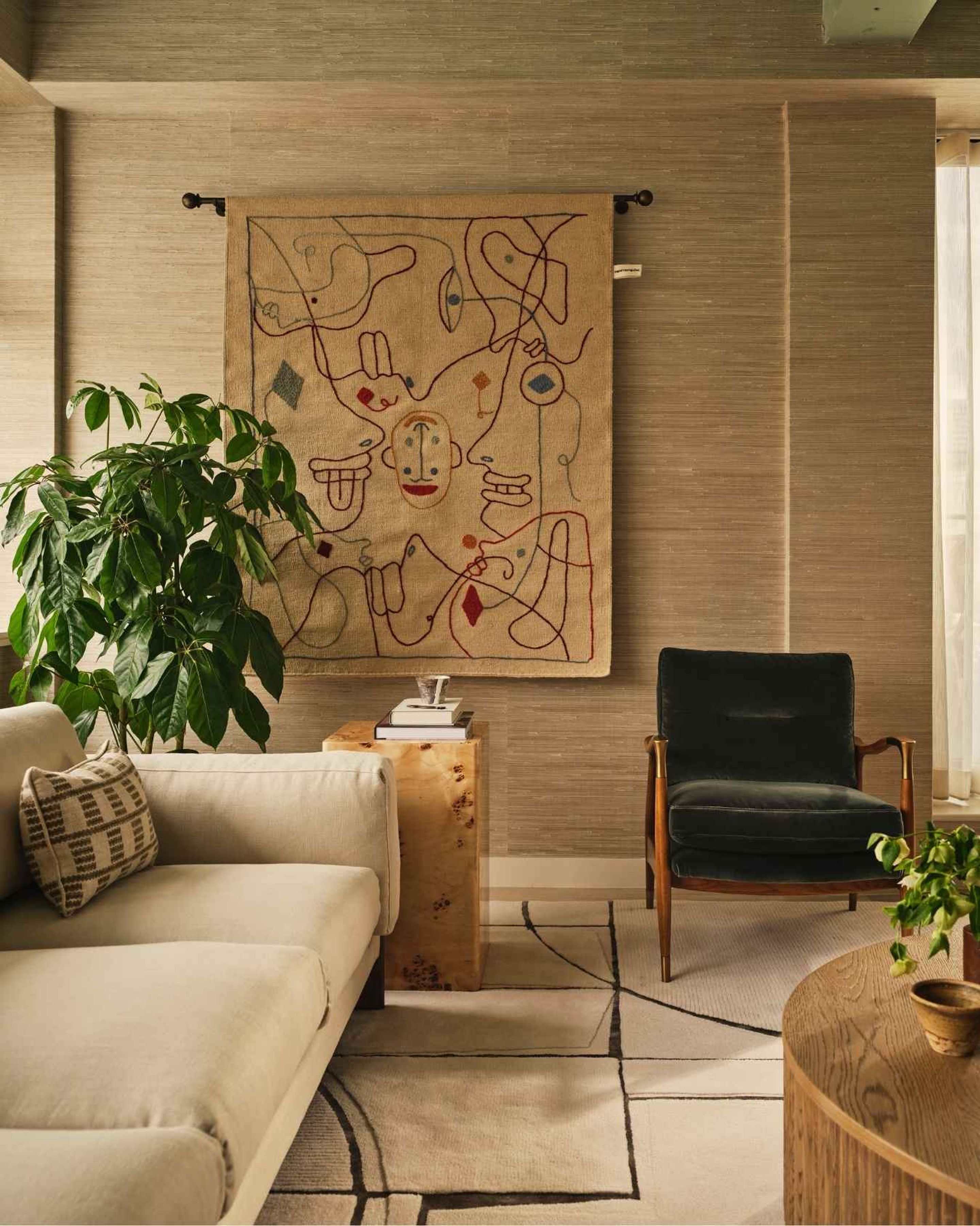 Sophisticated office lounge with cream sofa, dark green velvet armchair, bespoke rug and decorative wall tapestry.
