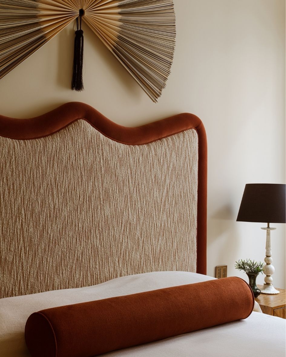 Bespoke upholstered bed with a sculptural terracotta headboard, textured fabrics and decorative fan-shaped wall art.