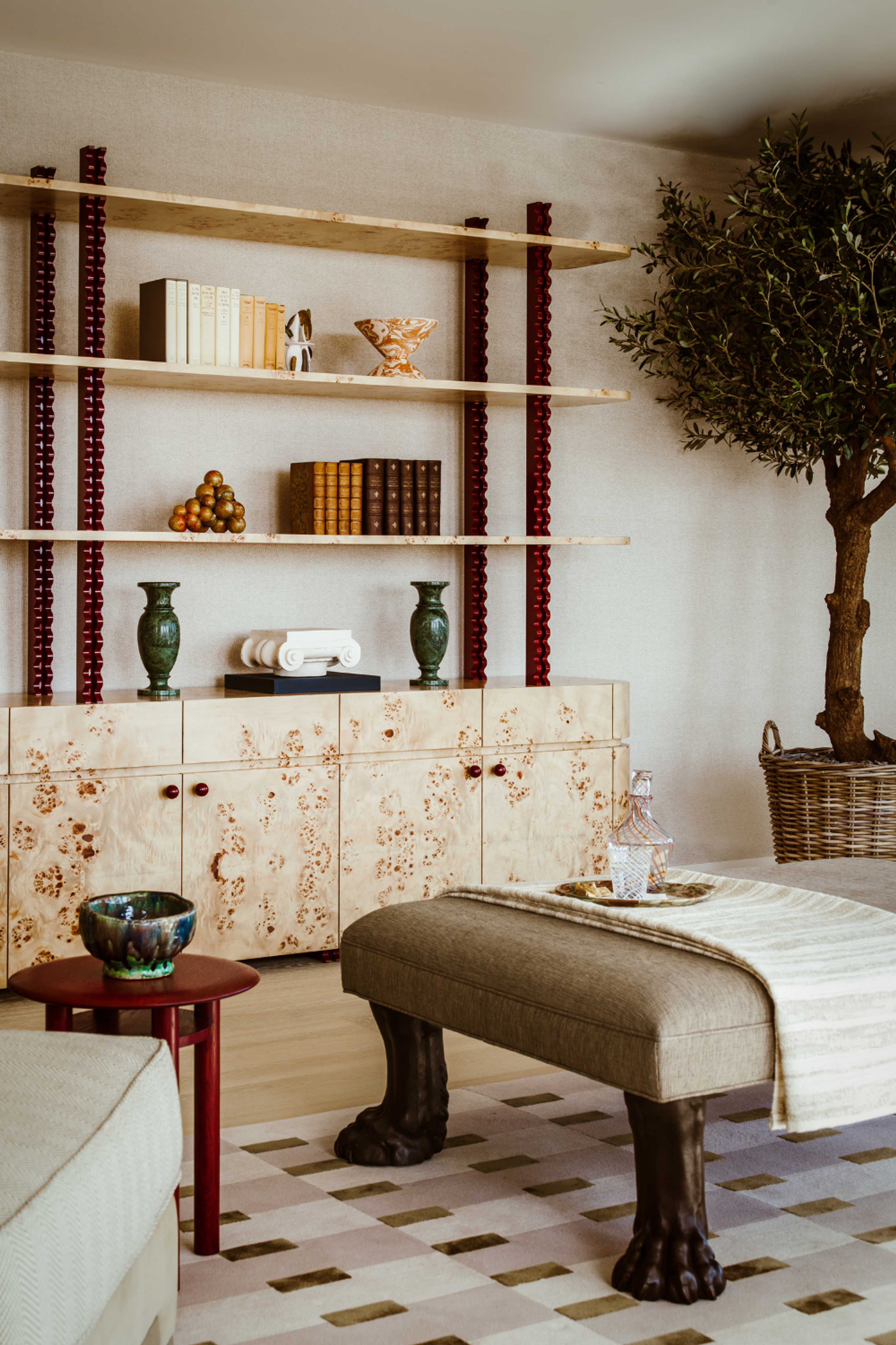 Burl wood cabinetry and open shelving styled with books, ceramics and antiques, creating a layered and characterful living space.