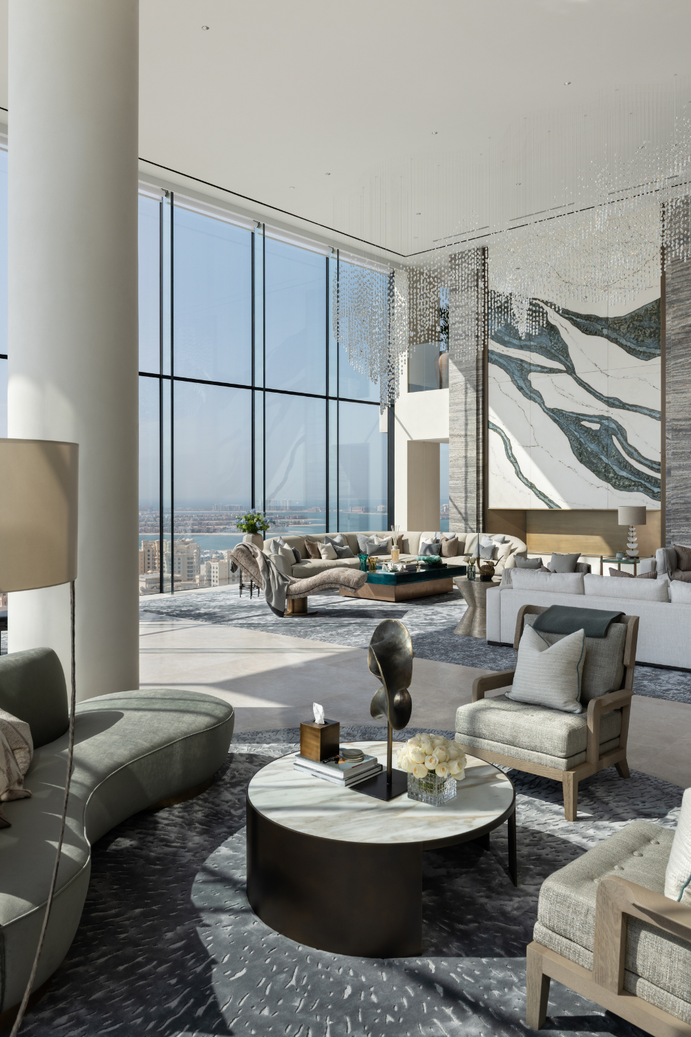 Double-height luxury Dubai penthouse living room with floor-to-ceiling glazing, sculptural seating, crystal chandeliers and a dramatic stone feature wall.