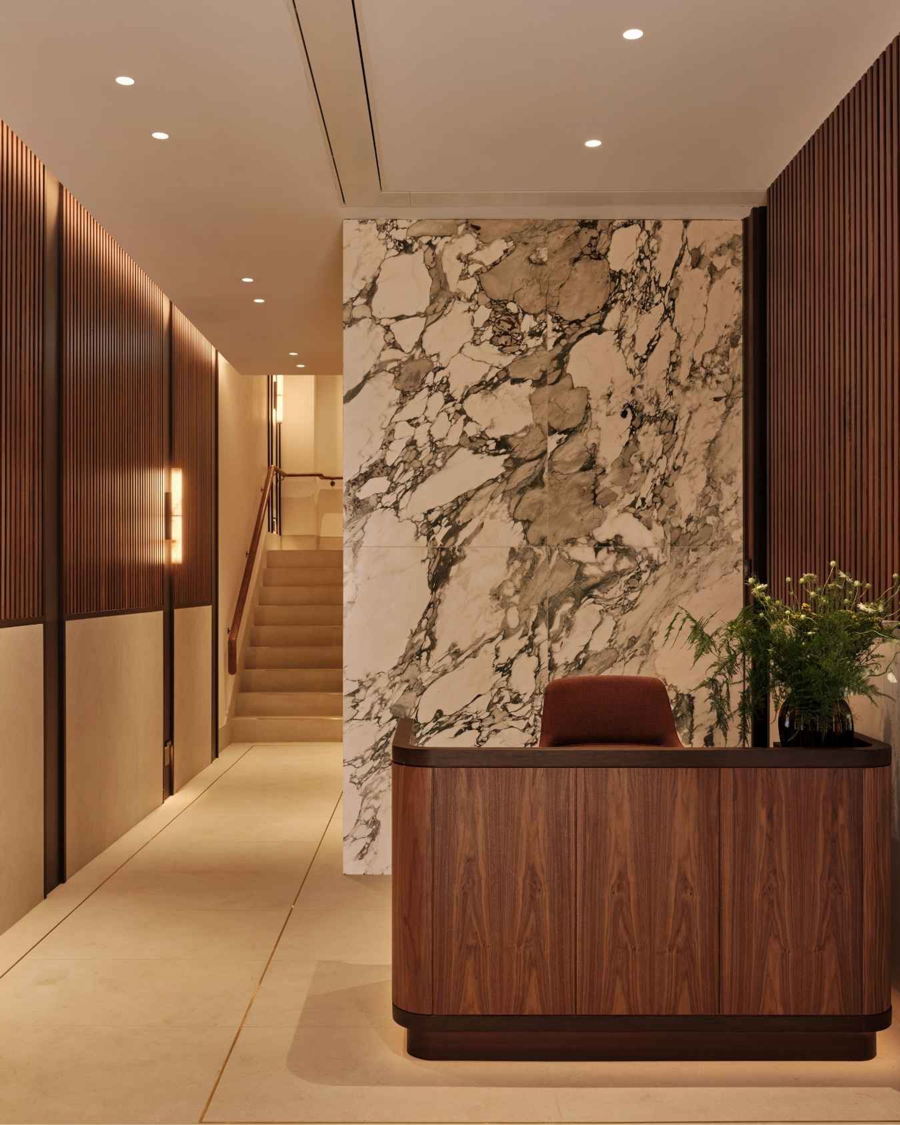 Luxury office reception featuring a curved walnut desk, dramatic marble feature wall and warm architectural lighting.