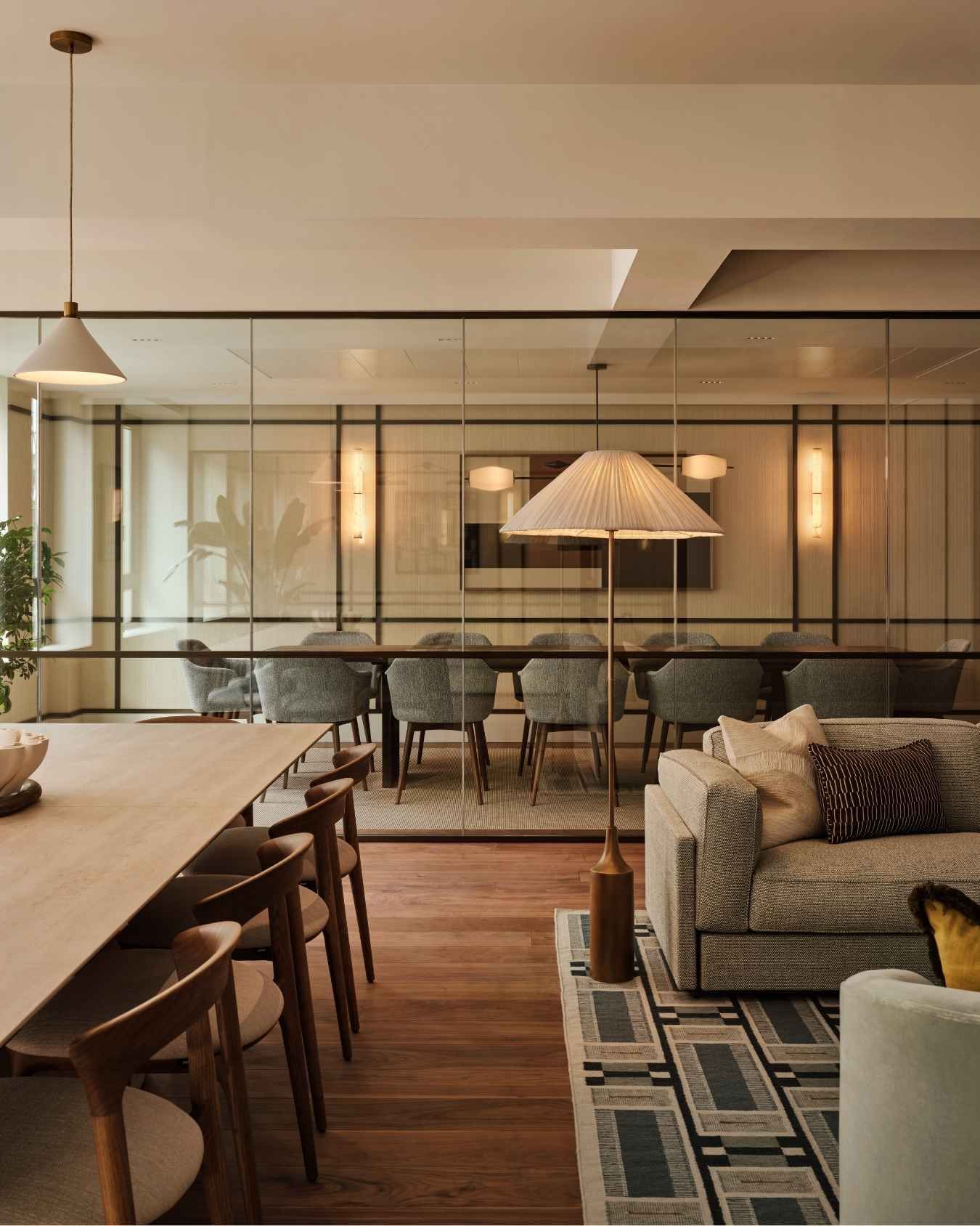 Luxury office lounge with communal dining table, upholstered seating, statement lighting and glass-partitioned meeting room.