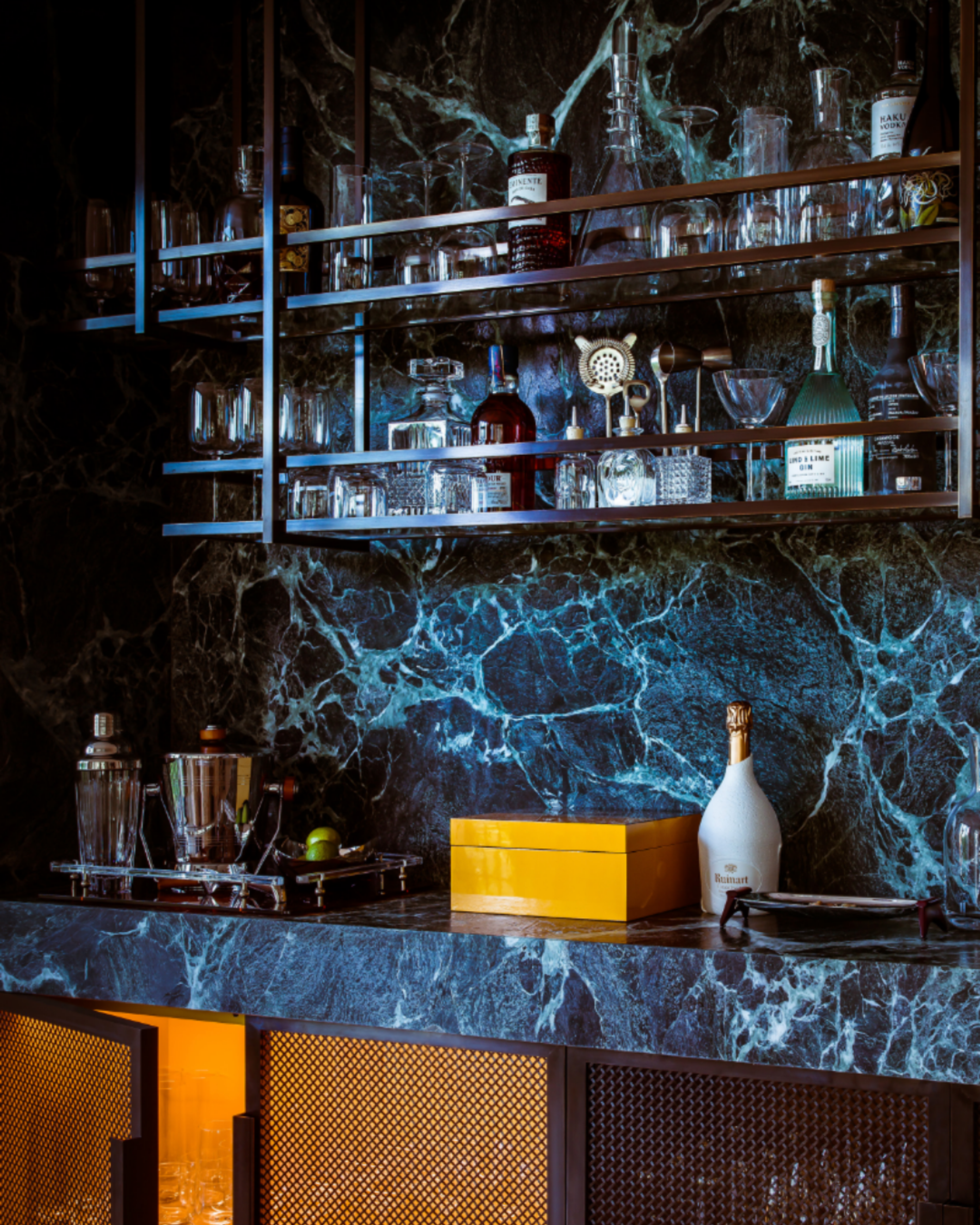 Private residential bar featuring dramatic blue-veined marble, bronze shelving, integrated lighting and a curated drinks display.