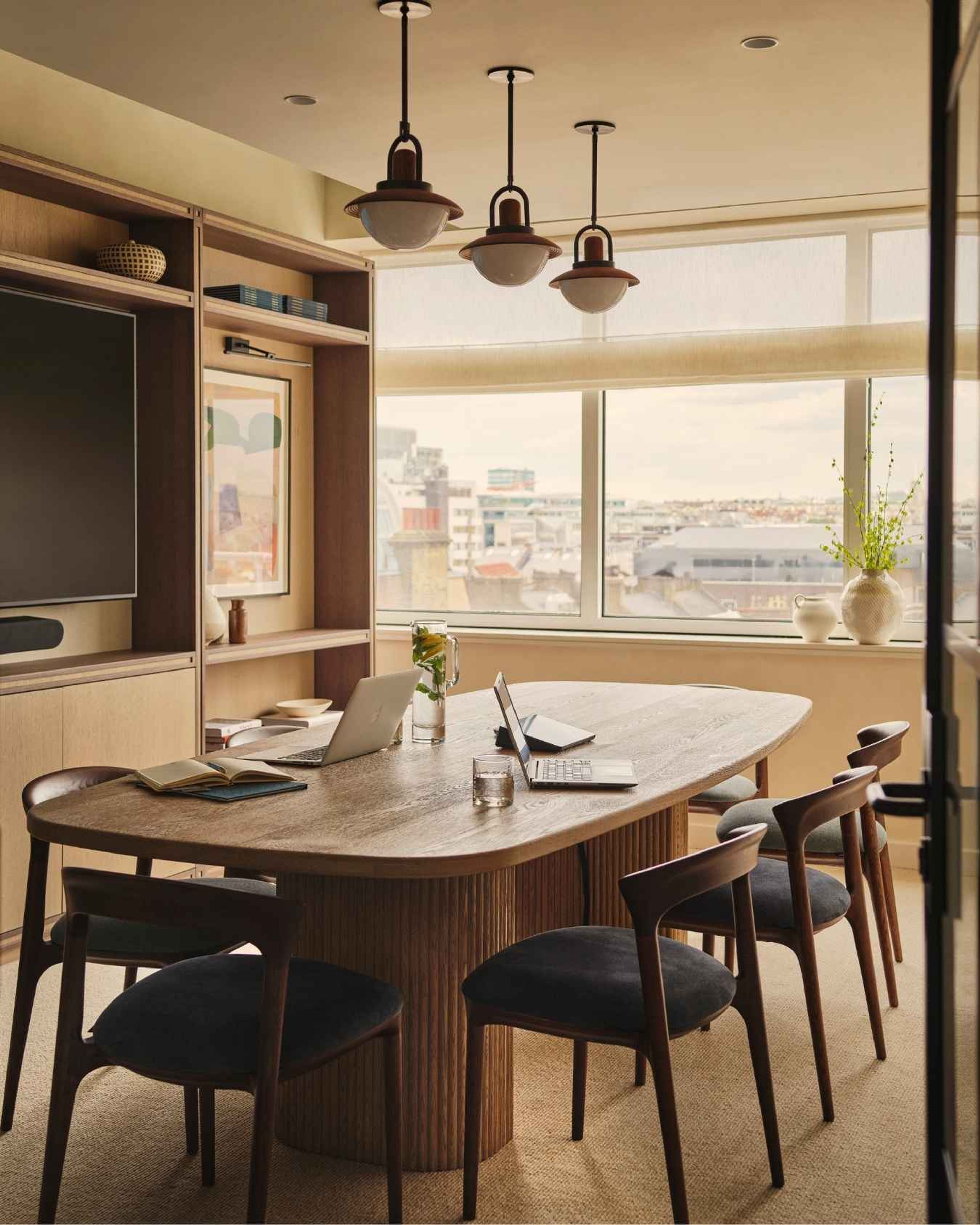 Contemporary meeting room featuring a bespoke timber conference table, upholstered chairs, pendant lighting and city views.