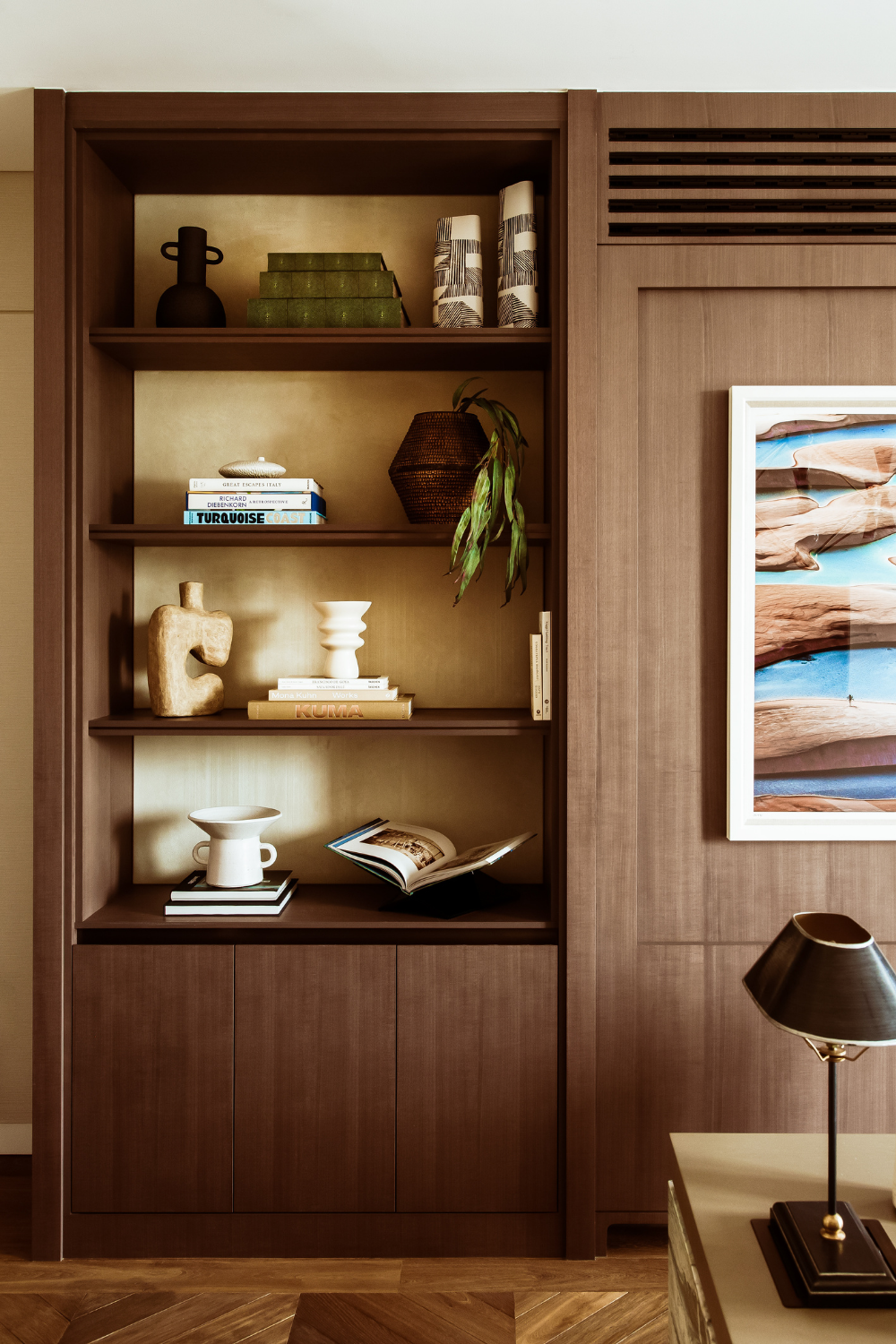 Custom timber shelving with brass-backed niches, curated books and decorative objects, creating a warm and tailored workspace.