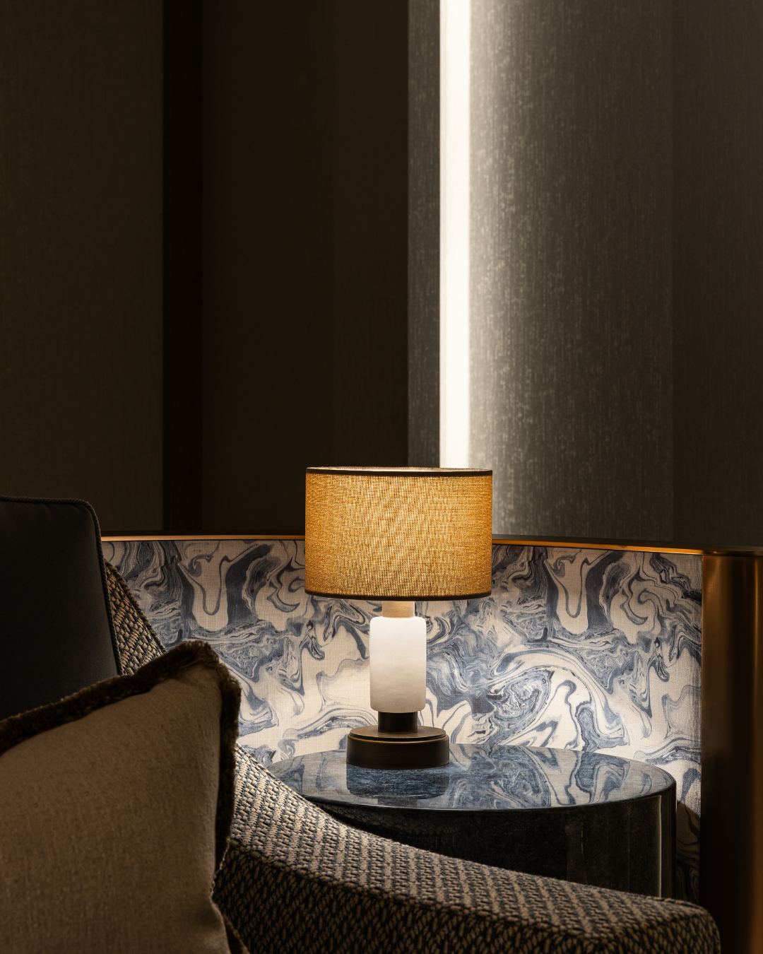 Cinema room detail with travertine-effect wallpaper, sea-blue marble fabric panelling, sculptural table lamp and low, ambient lighting.
