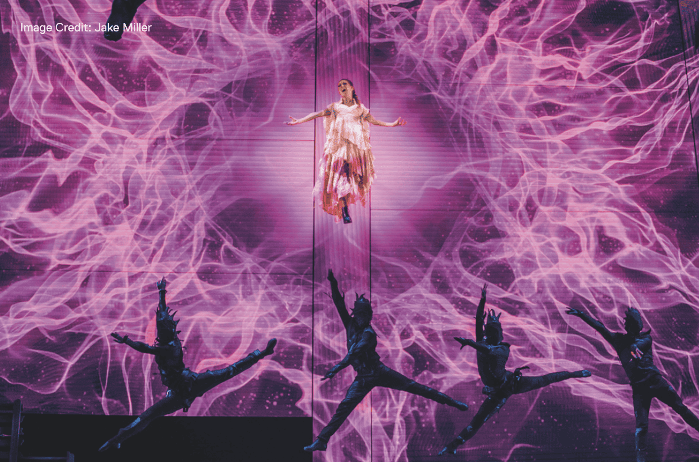 performer on stage surrounded by purple lights 