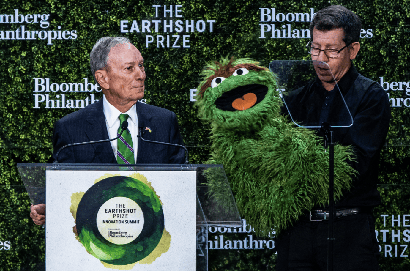 two men on stage speaking with a muppet