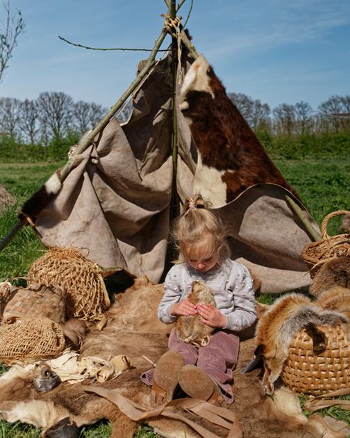 Meisje zit voor tent Hunebedcentrum in Borger, bestudeert een stukje prehistorisch bont