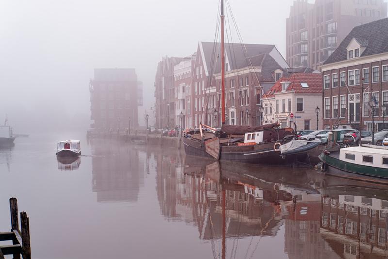 Thorbeckewal in Zwolle op een mistige winterochtend. Rechts antieke klippers en links een eenzaam bootje met witte opbouw.