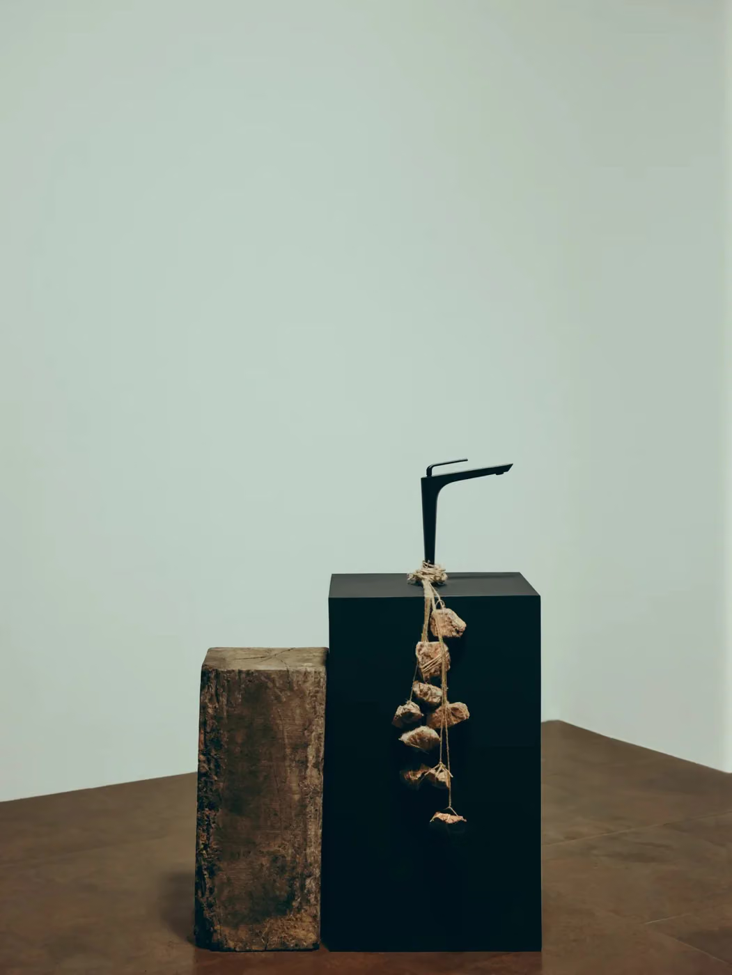 Black basin mixer standing on a black plinth beside a rough wooden block