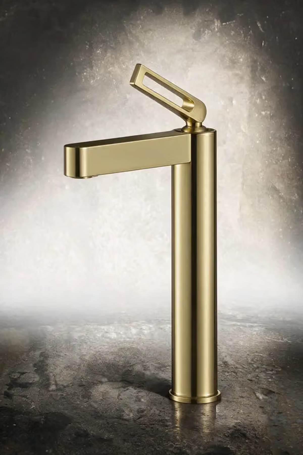 Brushed gold tall basin mixer with an open loop handle against a textured grey backdrop