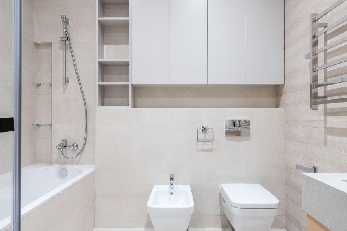 Compact bathroom with a wall-hung toilet and bidet beneath built-in cabinets, with a bathtub and heated towel rail