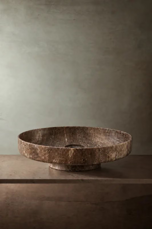 Low textured brown stone vessel basin on a stone shelf
