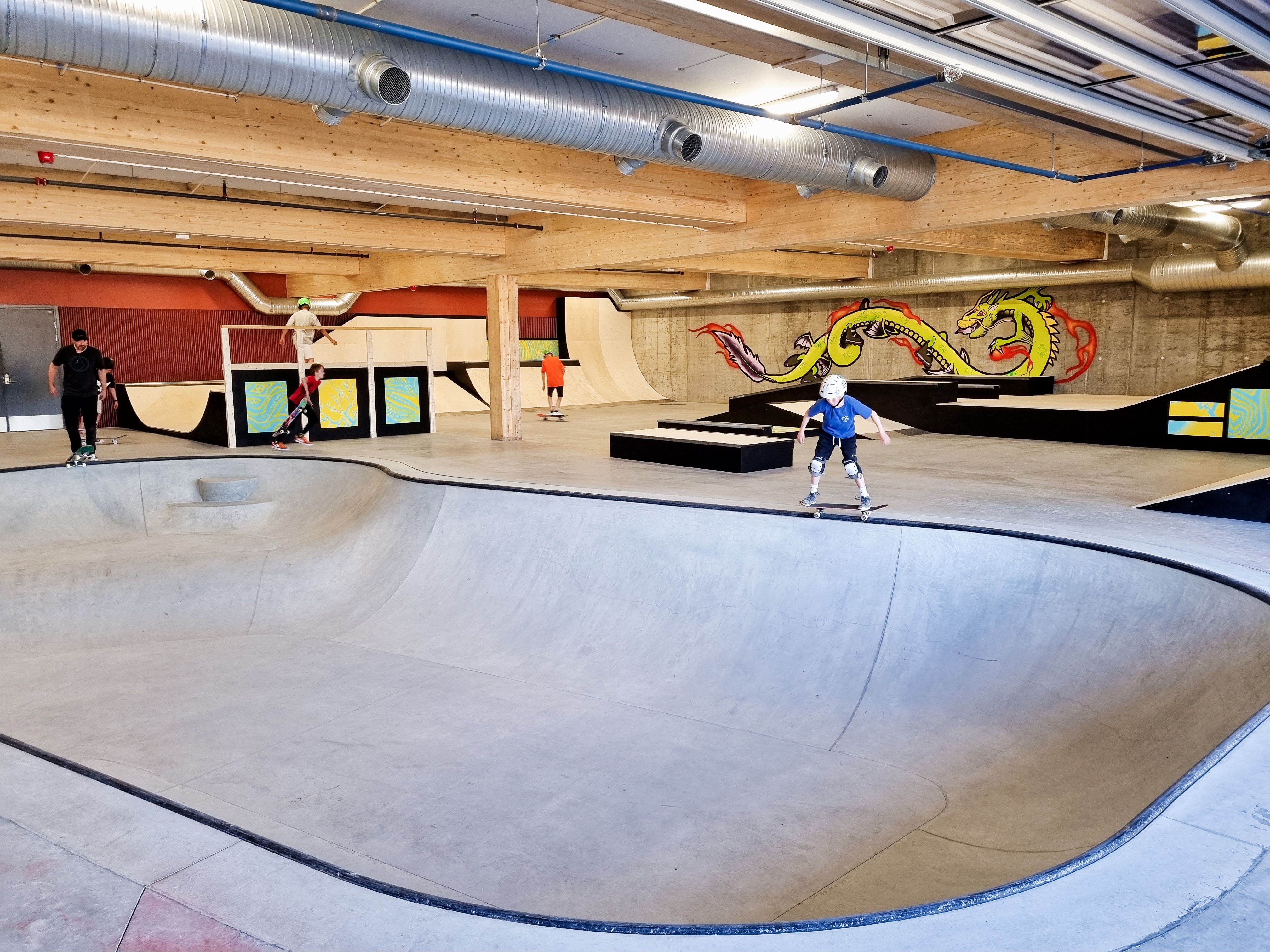 Barn og voksne skater i en innendørs skatehall. 