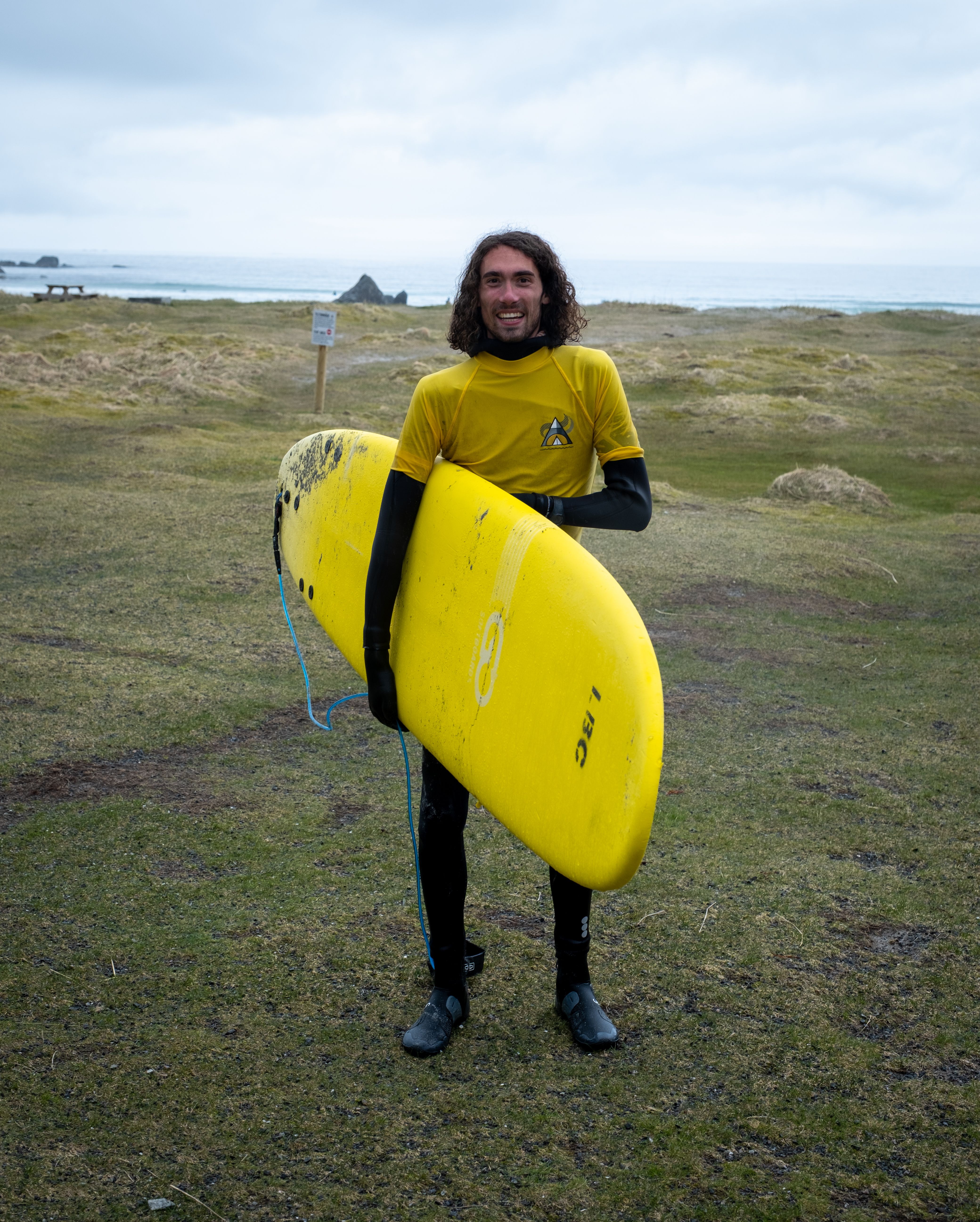Julien Simoens står med et gult surfebrett på stranden. 