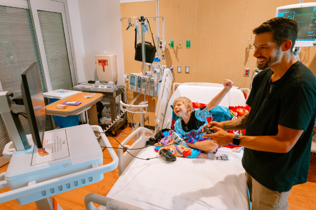 A kid celebrates in glee as he plays video games with an adult at a hospital