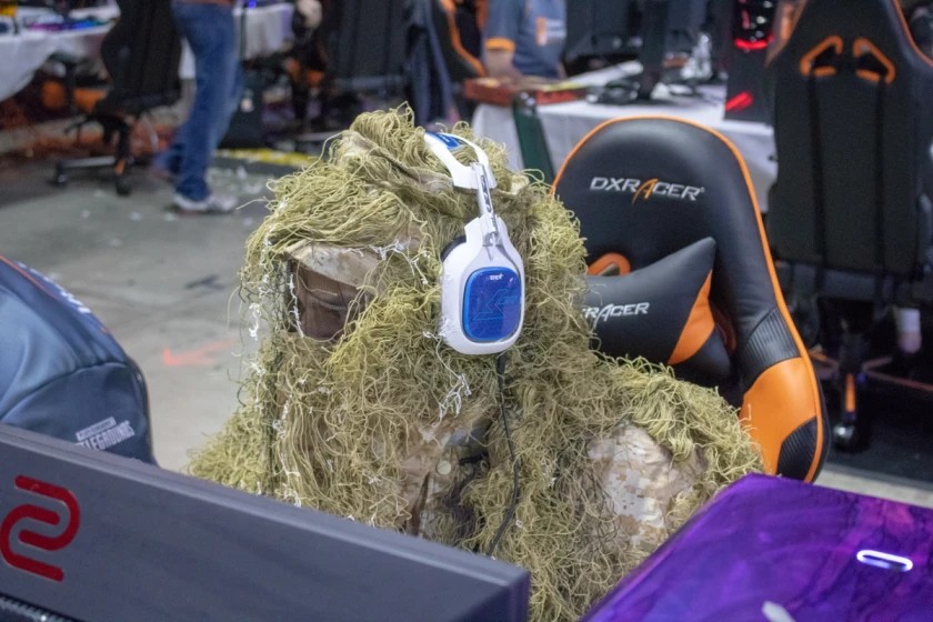 A person at their LAN station dressed up in a ghillie suit while wearing a headset.