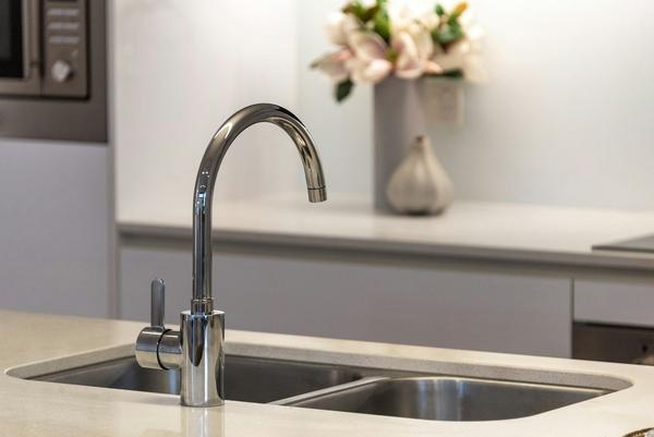 A chrome swan-neck kitchen tap over a stainless steel sink.