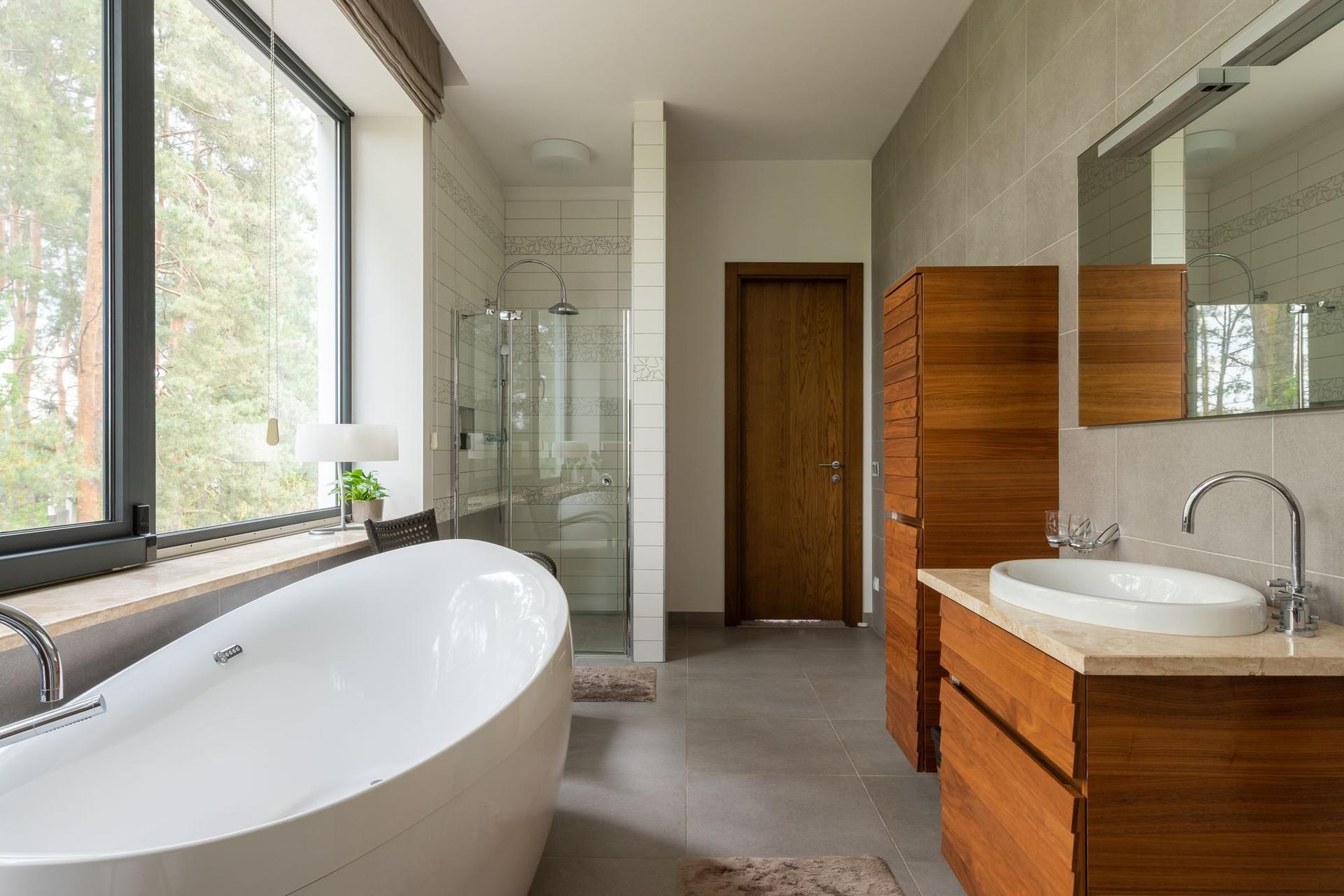 A newly finished bathroom with a white bath, wooden vanity unit and large window.