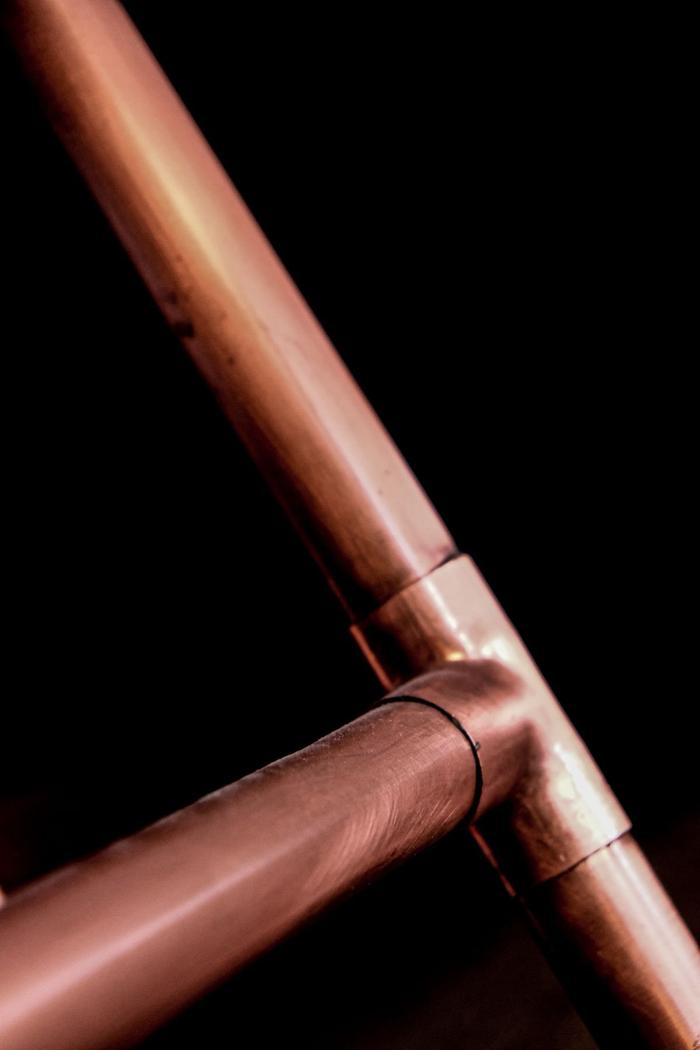 Copper pipes joined at a T-junction against a dark background.