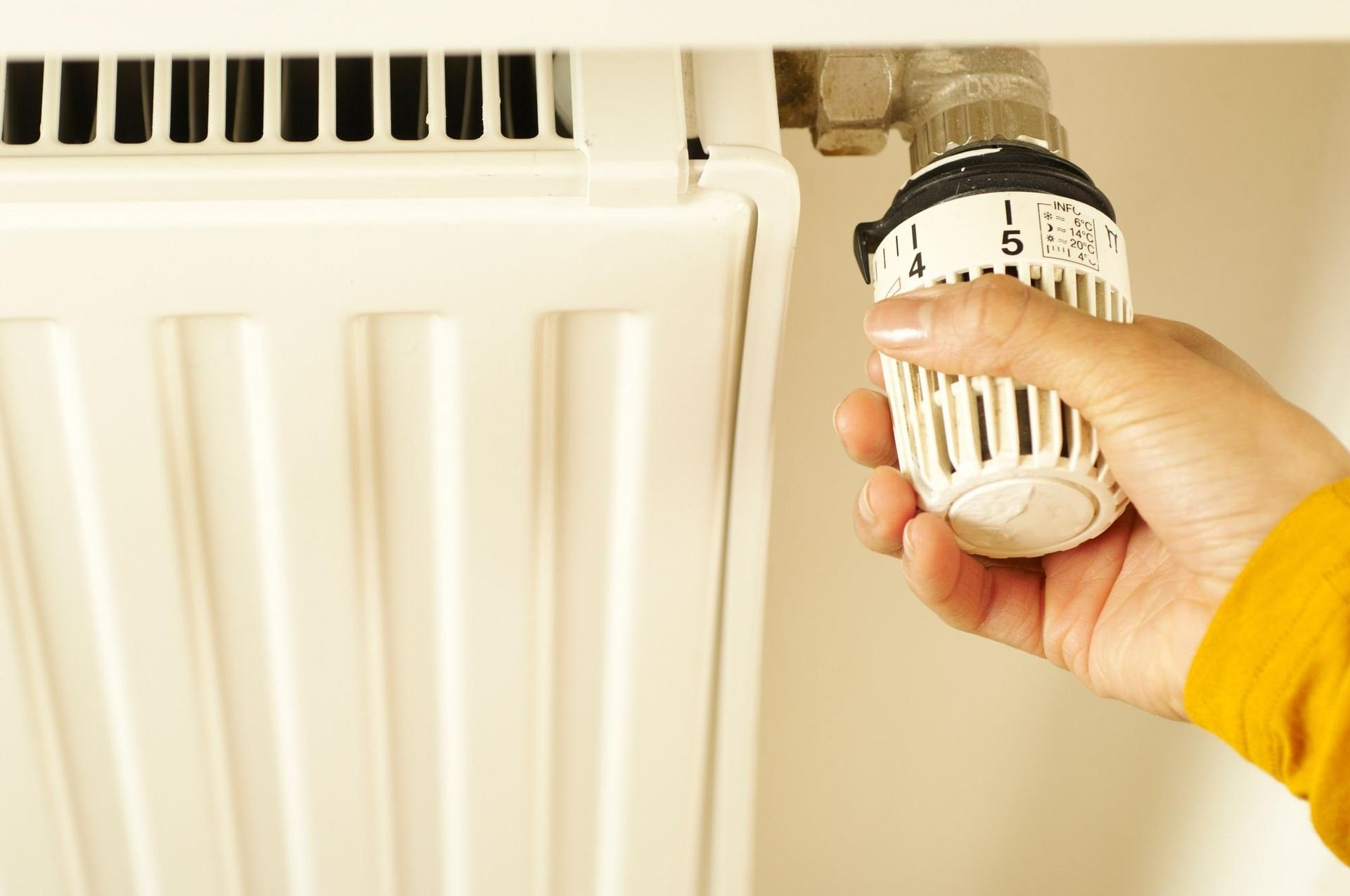 A hand turning the thermostatic valve on a white radiator.