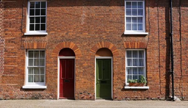Two brick terraced houses with red and green front doors.