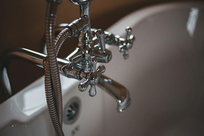 A chrome bath mixer tap with shower handset on a white bath.