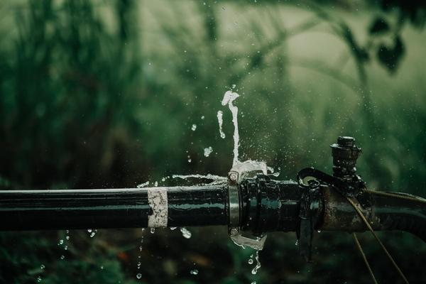 Water spraying out of a leaking joint on a black water pipe.