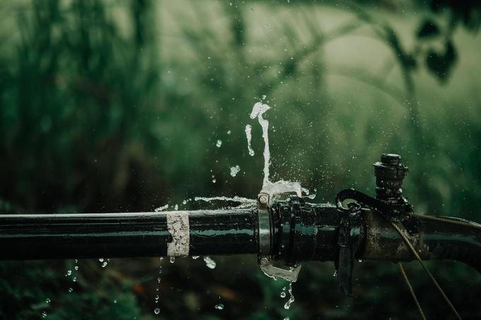 Water spraying out of a leaking joint on a black water pipe.
