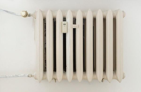 A white cast-iron column radiator with a thermostatic valve on a plain wall.