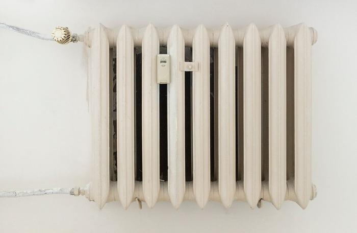A white cast-iron column radiator with a thermostatic valve on a plain wall.