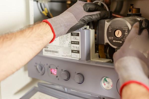 Gloved hands working on the pump inside a gas boiler with its front casing removed.
