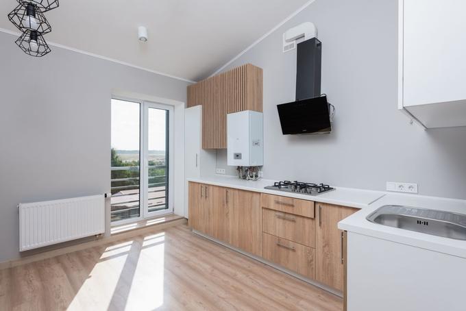A newly fitted white wall-mounted boiler in a bright kitchen, with a radiator under the window.